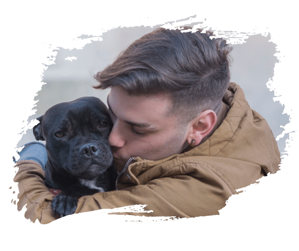 A young man in a brown jacket lovingly hugging and kissing a black dog with a calm expression.